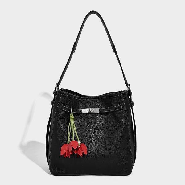 Soft-structured pebbled bucket shoulder bag with front turn-lock strap detail, adjustable strap, and hanging floral tassel