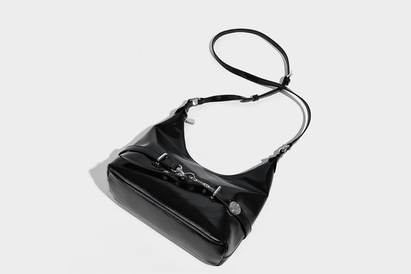 Glossy black slouchy hobo shoulder bag with silver-tone hardware, belt-style grommet strap at base, and long adjustable