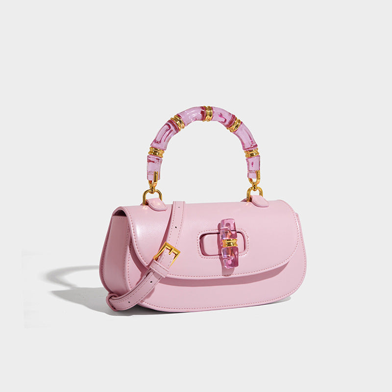 Small structured saddle bag with translucent pink resin bamboo-style top handle, matching front turn-lock clasp, gold-tone