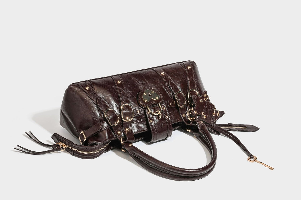 Glossy dark brown structured Boston satchel with heart-shaped lock charm, star pendant, rivet studs, multi-strap front panel