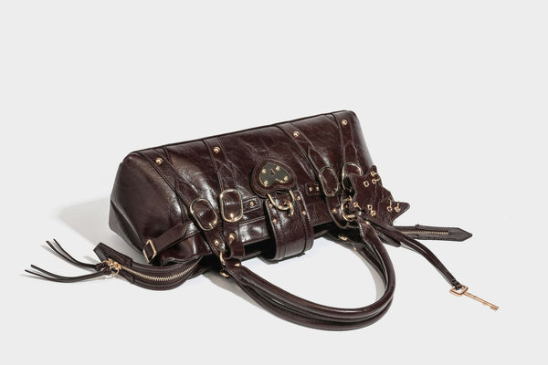 Glossy dark brown structured Boston satchel with heart-shaped lock charm, star pendant, rivet studs, multi-strap front panel