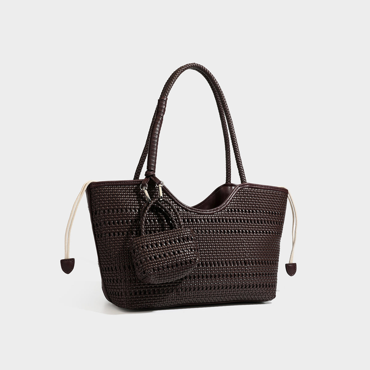 Structured woven tote bag in dark brown with braided handles, drawstring side ties, and attached mini woven pouch with, front