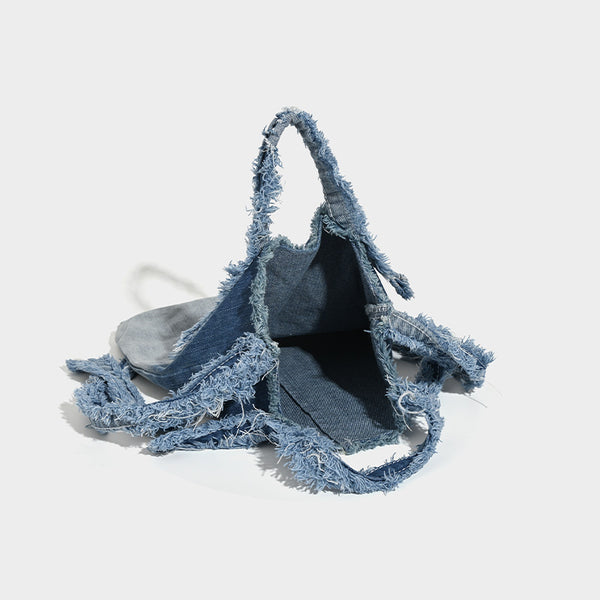 Washed denim fringe crossbody bag with indigo-to-pale-blue gradient and raw fringe trim along edges and shoulder strap