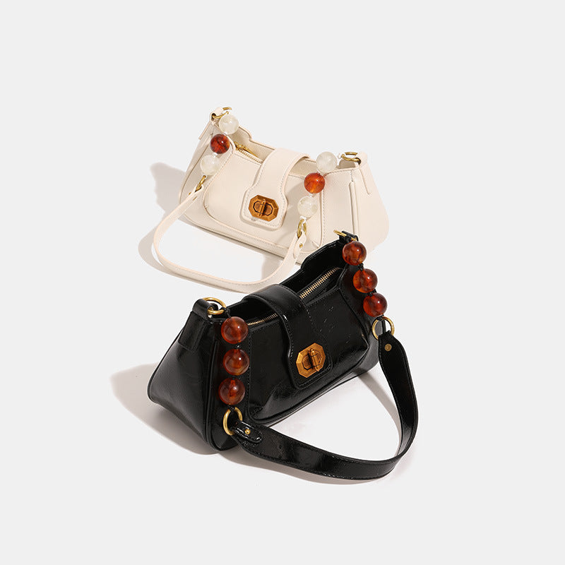 Structured glossy crinkled-finish shoulder bag with amber resin bead strap accent and gold-tone turn-lock closure, detail