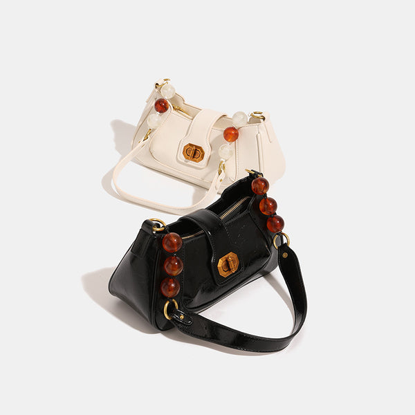 Structured glossy crinkled-finish shoulder bag with amber resin bead strap accent and gold-tone turn-lock closure, detail