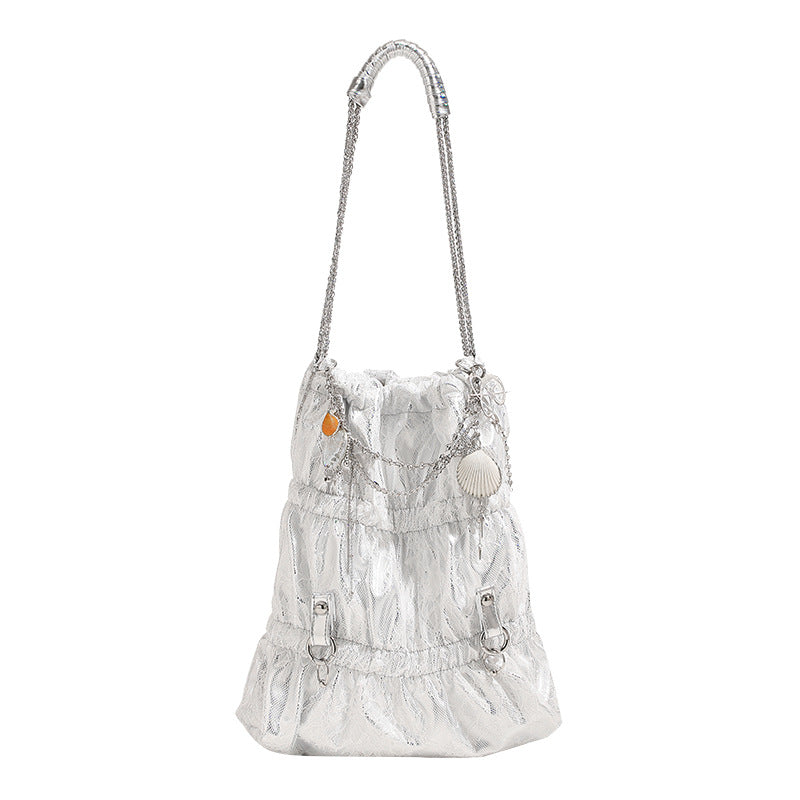 Slouchy lace-overlay bucket bag with silver chain strap, draped chain detail, shell charms, and drawstring top closure