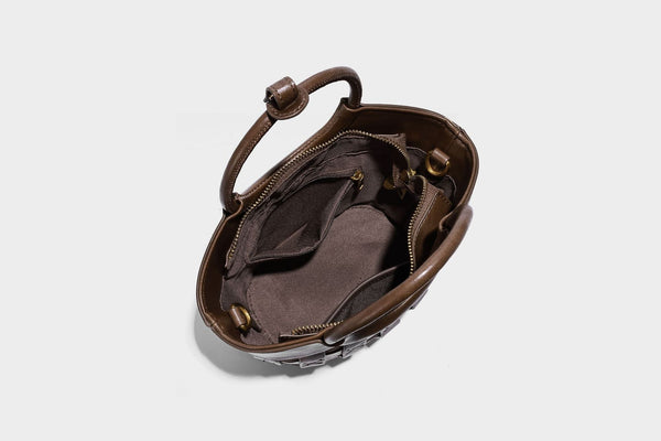 Small woven-panel bucket bag with circular ring handles, beaded tassel charm, and detachable crossbody strap in brown, detail