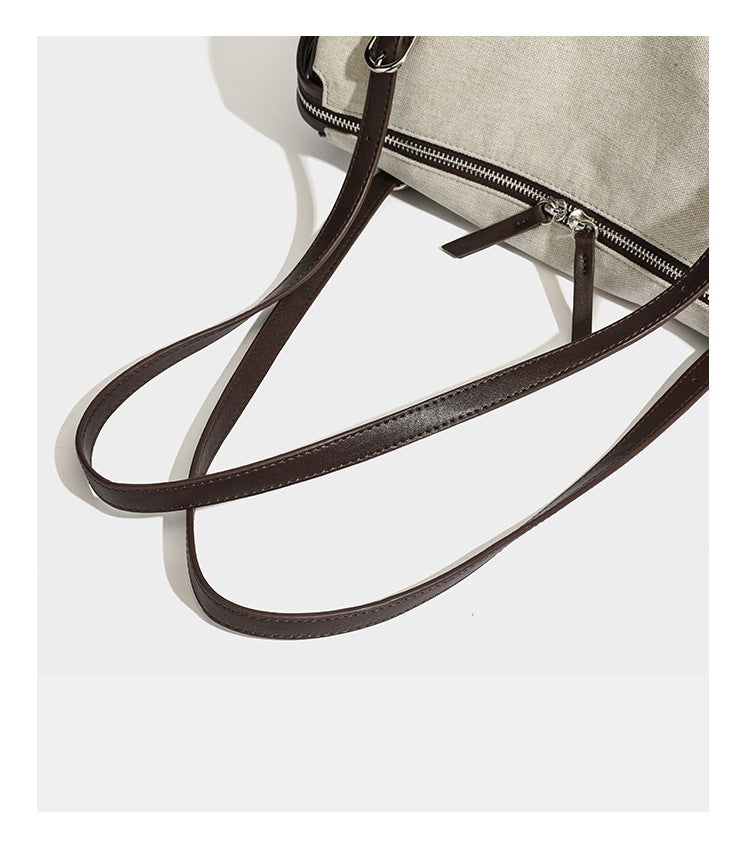 Beige canvas barrel bag with dark brown leather-look trim, silver-tone hardware, top zip closure, and adjustable shoulder