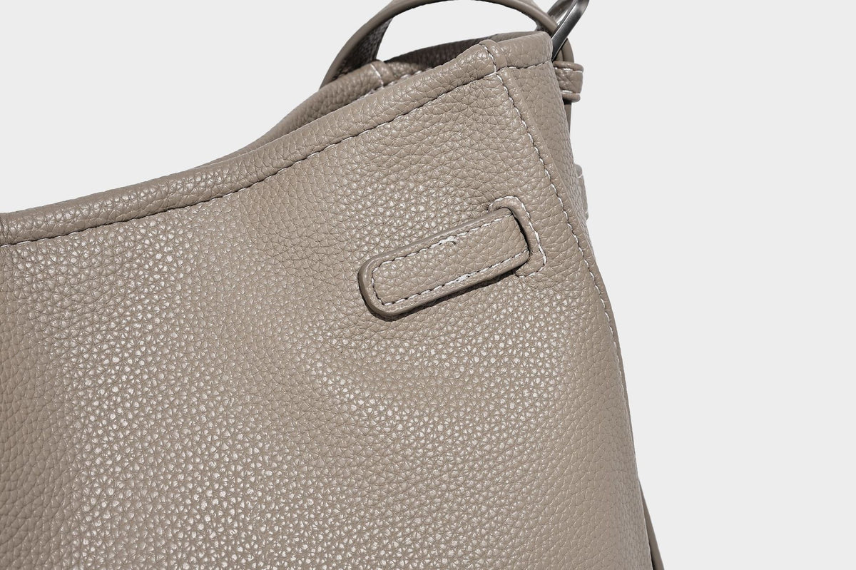 Soft-structured pebbled bucket shoulder bag with front turn-lock strap detail, adjustable strap, and hanging floral tassel