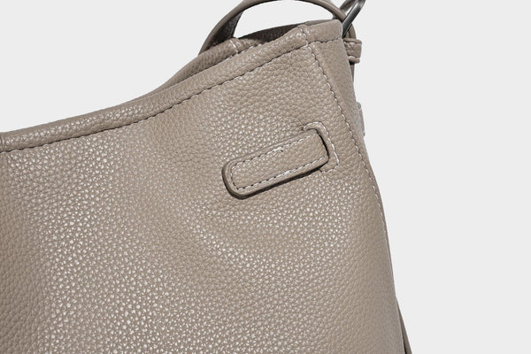 Soft-structured pebbled bucket shoulder bag with front turn-lock strap detail, adjustable strap, and hanging floral tassel