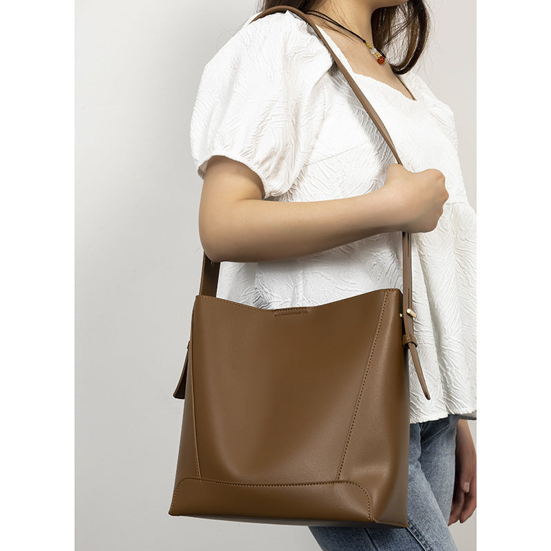 Structured smooth leather-look bucket shoulder bag with long adjustable strap and gold-tone buckle hardware in brown, detail
