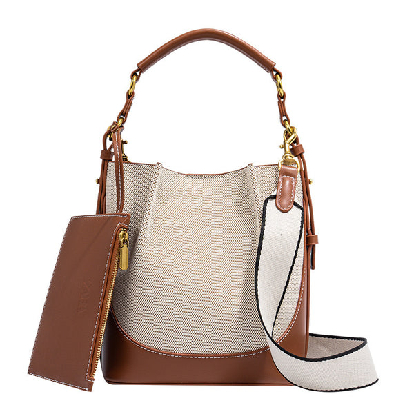 Cream canvas and tan leather-look bucket bag with arched top handle, wide detachable shoulder strap, and gold-tone hardware