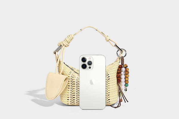 Small woven crescent shoulder bag with leather-look trim, zip closure, silver-tone ring hardware, and beaded tassel charm