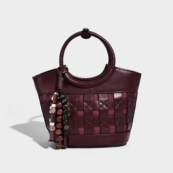 Small woven-panel bucket bag with circular ring handles, beaded tassel charm, and detachable crossbody strap in brown, detail