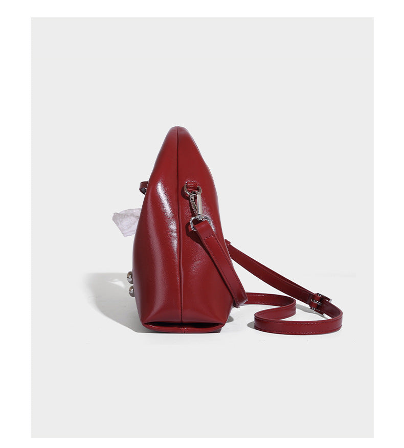 Kleine kuppelförmige Henkeltasche in glänzender Lederoptik mit Kordelzugverschluss, weißem Spitzen-Schleifenanhänger und silberfarbenen Metallbeschlägen