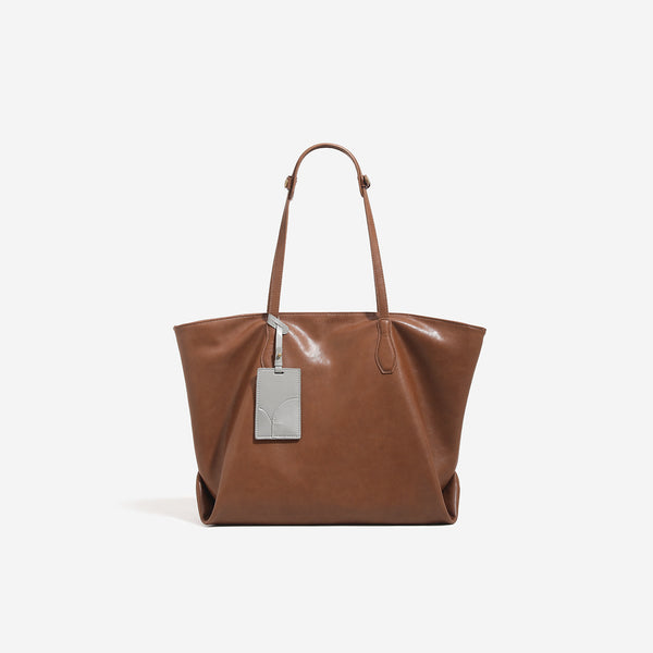 Oversized slouchy leather-look tote bag with long shoulder straps, contrast grey hanging tag, and silver-tone hardware