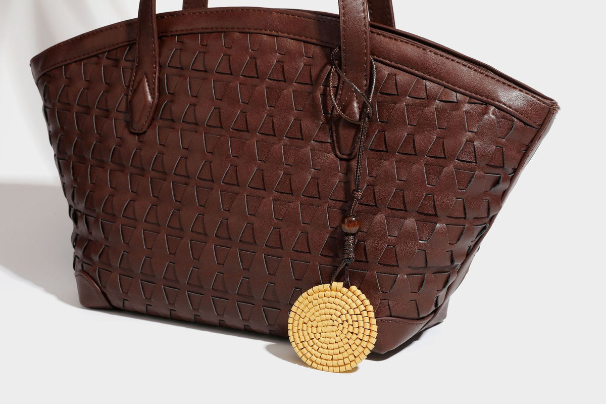 Large leather-look tote bag with geometric woven emboss, double shoulder straps, and round woven cord charm in brown, detail
