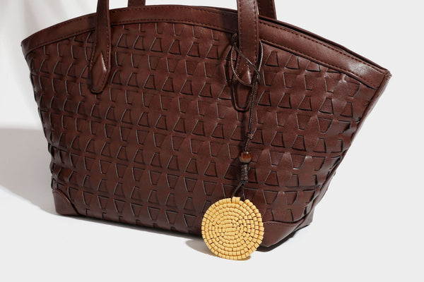 Large leather-look tote bag with geometric woven emboss, double shoulder straps, and round woven cord charm in brown, detail