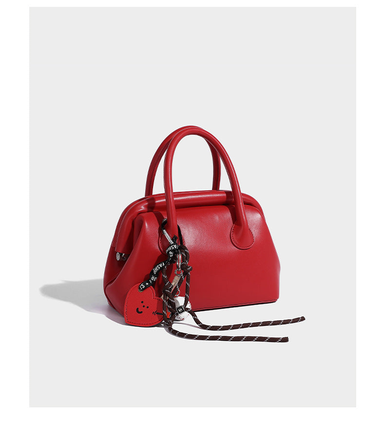 Small structured shell top-handle bag in red with heart charm and braided cord detail, smooth leather-look finish, detail