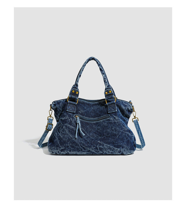 Large washed blue denim-look shoulder bag with gold-tone rings and rivets, top zip closure, front zip pocket, and adjustable