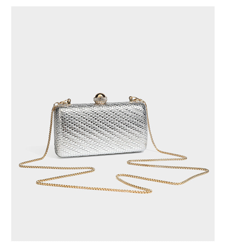 Small structured metallic woven-texture box clutch bag with jeweled kiss-lock dome clasp and slim gold chain strap, detail