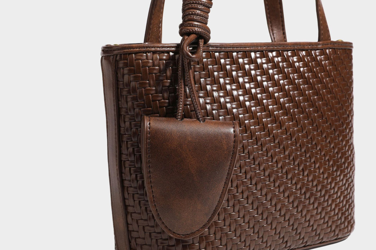 Strukturierte Tote Bag mit gewebter Oberfläche in Braun, goldfarbenen Metalldetails, seilumwickelten Tragegriffen, einer kleinen Fronttasche und weiteren Details