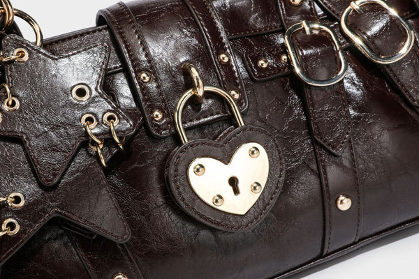 Glossy dark brown structured Boston satchel with heart-shaped lock charm, star pendant, rivet studs, multi-strap front panel