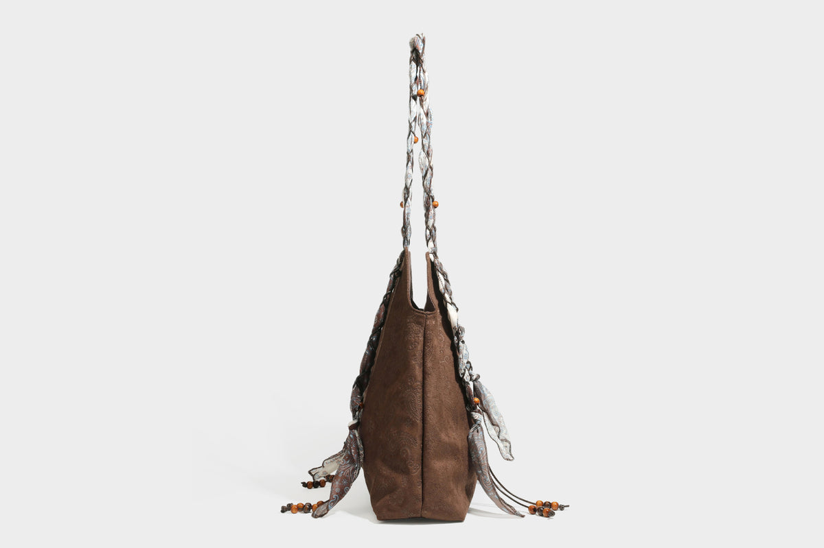 Slouchy paisley-embossed suede-look shoulder tote bag with braided patterned fabric straps and wood bead accents, detail view