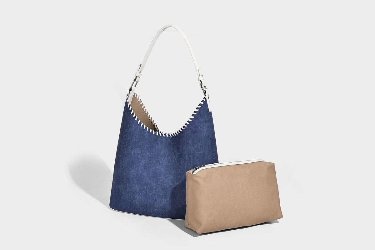 Denim-blue hobo tote with white leather-look shoulder strap, contrast whipstitch trim along curved open top, and silver-tone