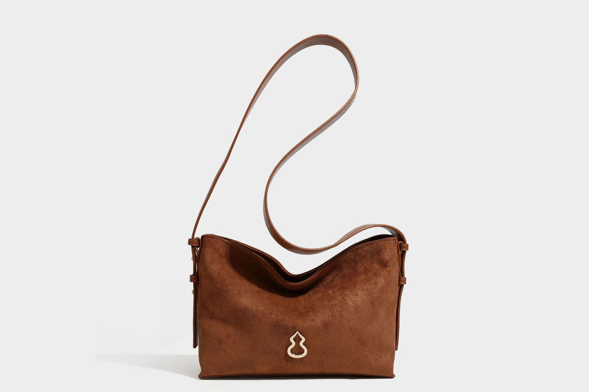 Slouchy suede-finish brown shoulder bag with long single strap and small gold-tone logo emblem on front, detail view 29