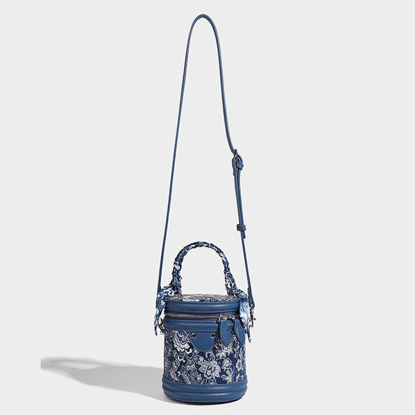 Small cylindrical barrel bag in blue-and-white floral jacquard with leather-look trim, scarf-wrapped top handle, silver-tone