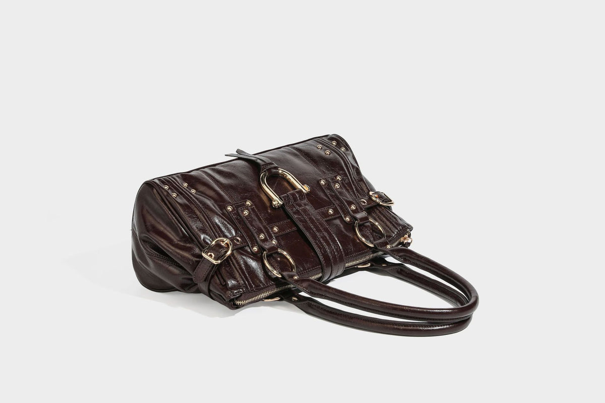 Glänzende Henkeltasche in Lederoptik mit zwei oberen Henkeln, goldfarbenen Nieten- und Ringbeschlägen, einem Riemendetail mit Schnalle auf der Vorderseite und
