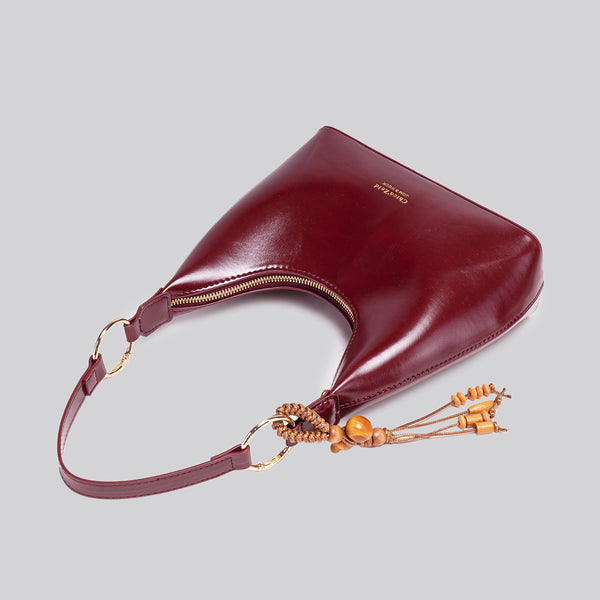 Glossy crescent hobo shoulder bag in deep burgundy with beaded wood tassel charm and gold-tone ring hardware, detail view 4