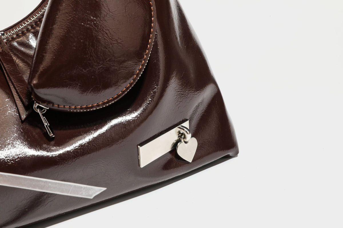 Weich fallende Hobo-Schultertasche in glänzender Lederoptik mit silberfarbenen Ösen zum Schnüren und Schleifenband auf der Vorderseite, Detailansicht