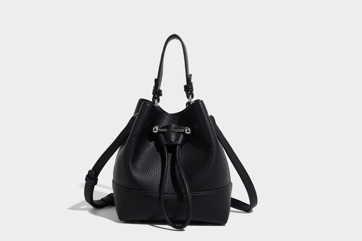 Small two-tone pebbled drawstring bucket bag with tan contrast base, metal toggle hardware, short top handle, and detachable