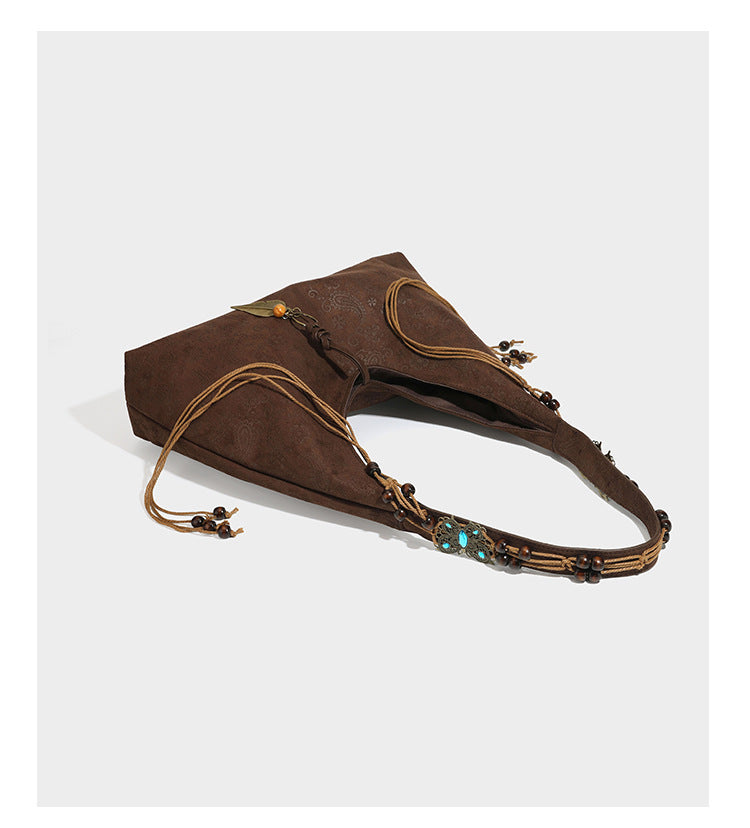 Slouchy boho hobo shoulder bag in embossed brown suede-look finish with beaded strap, cord tassels, and brass-tone leaf