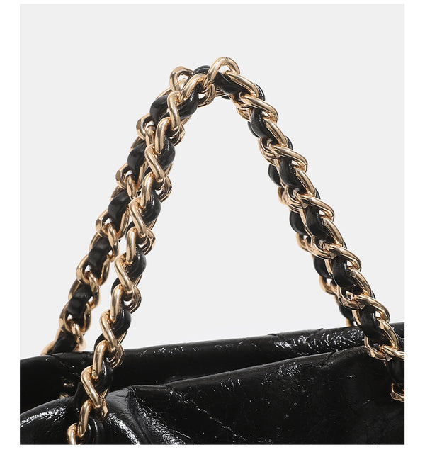 Black glossy diamond-quilted bucket tote bag with gold-tone chain accent, turn-lock front flap pocket, drawstring side ties