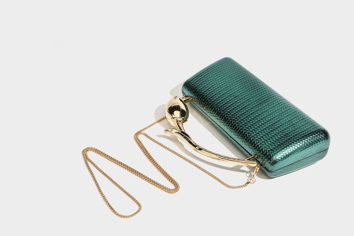 Structured rectangular metallic woven clutch bag with sculptural gold-tone leaf top handle and detachable chain strap, detail