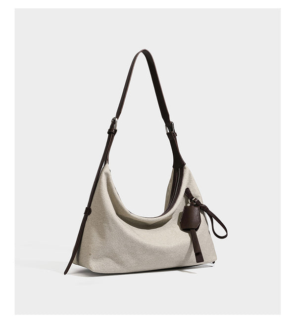 Cream canvas hobo shoulder bag with dark brown leather-look trim, zip-top closure, adjustable strap, and silver-tone