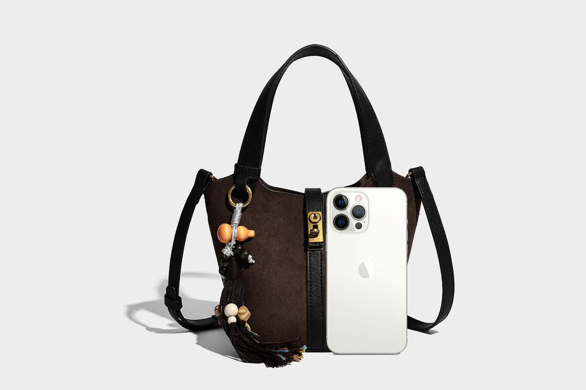 Small structured trapezoid tote bag in matte suede-look finish with black contrast trim, gold-tone front clasp, tassel charm