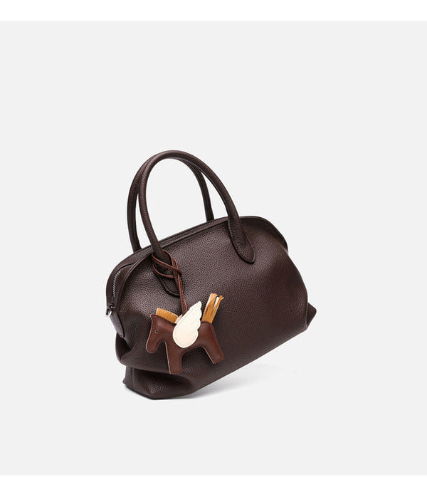 Rounded dome shell handbag in pebbled leather-look finish with twin top handles, zip closure, decorative horse charm, and