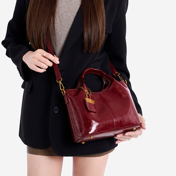 Structured crinkle-gloss top-handle satchel in deep burgundy with antique gold lock charm and detachable shoulder strap