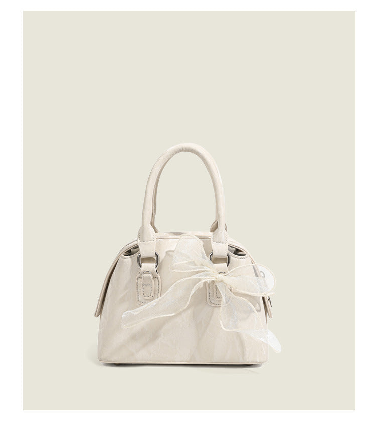 Small structured Boston bag in cream with glossy crinkled finish, sheer bow accent, silver-tone hardware, dual top handles