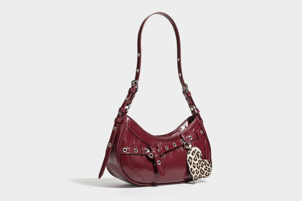 Kompakte, sichelförmige Schultertasche in glänzender bordeauxroter Lederoptik mit silberfarbenem Ösenschnallenriemen und Leopardenmuster