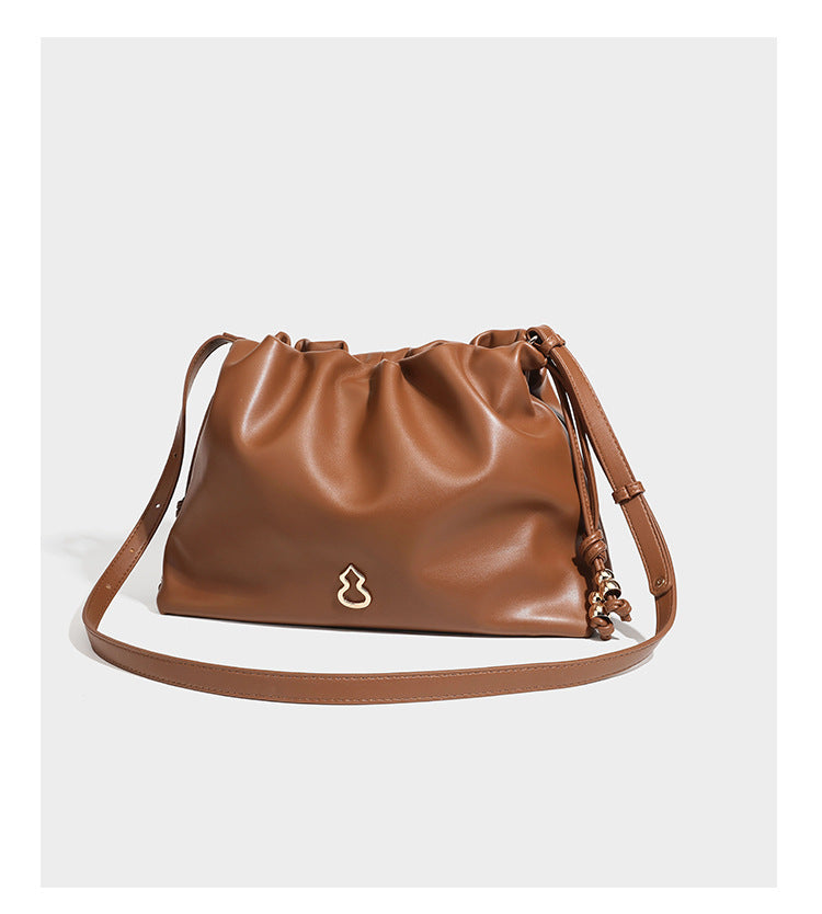 Slouchy ruched drawstring shoulder bag in smooth leather-look finish with gold-tone emblem and slim adjustable strap, detail