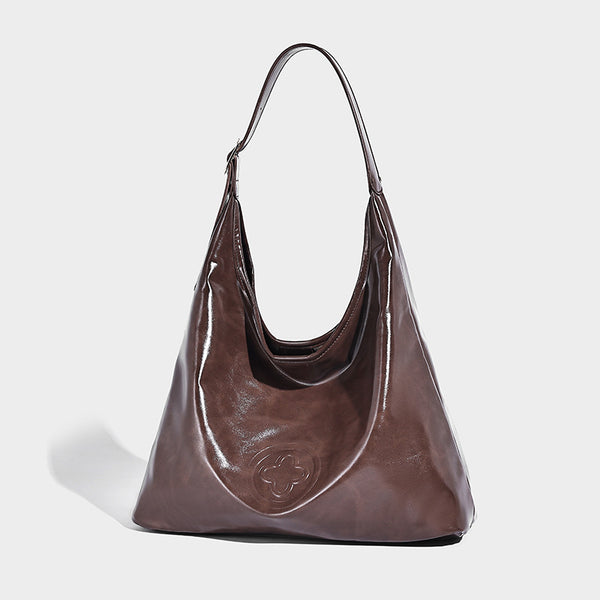 Glossy slouchy hobo shoulder bag with adjustable strap and embossed floral emblem, front view