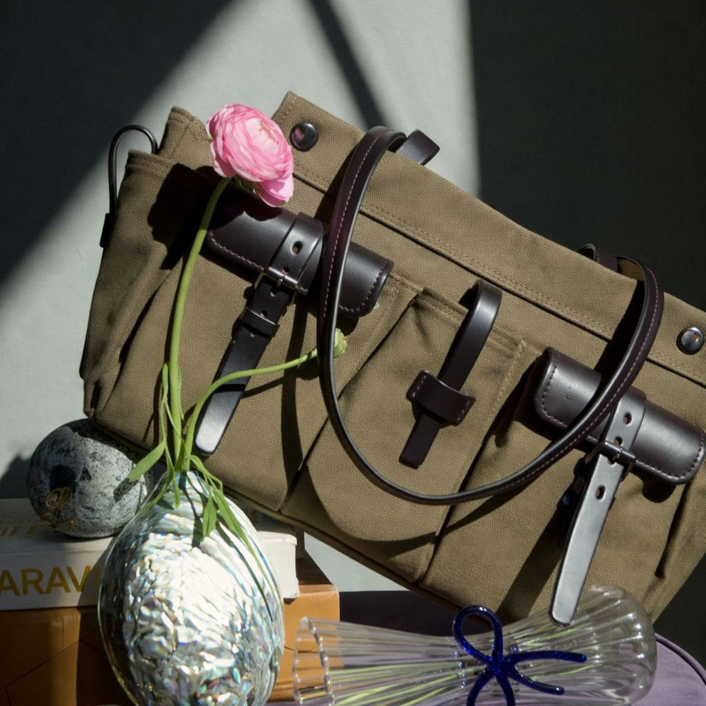 Großer olivgrüner Canvas-Schultershopper mit mehreren Vordertaschen mit Schnallenriemen und dunkelbraunem Besatz in Lederoptik, Vorderansicht