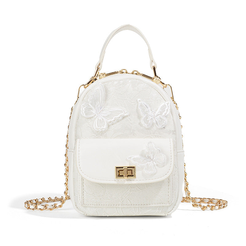 Structured mini backpack handbag with butterfly embroidery, gold-tone chain strap, and turn-lock front flap pocket, detail