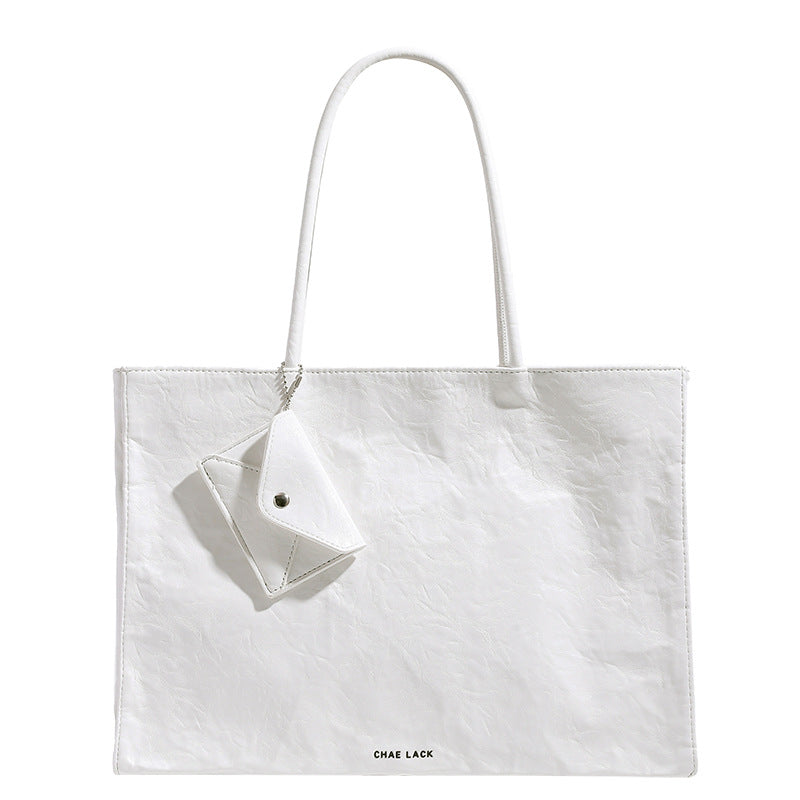 Structured rectangular crinkle leather-look tote bag with long rounded handles, zip top, and envelope-style hanging tag