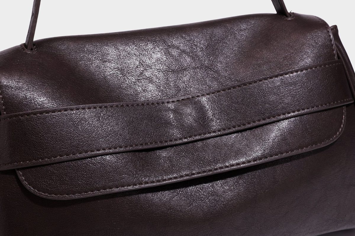Strukturierte rechteckige dunkelbraune Schultertasche in Lederoptik mit Klappe, mehrlagigem Detail auf der Vorderseite und langem verstellbarem Riemen, Detailansicht